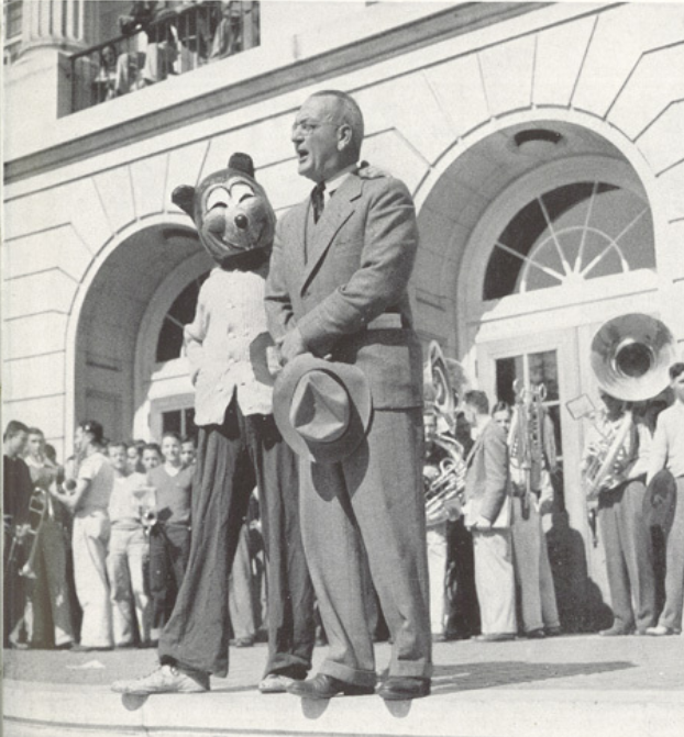 Archival scan: Oski beside a speaker and band outside a campus building. Photo credit: Photographer/artist uncredited in supplied scan.