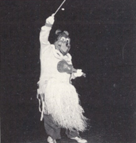 Archival scan: Oski wearing a grass skirt and raising a baton. Photo credit: Photographer/artist uncredited in supplied scan.