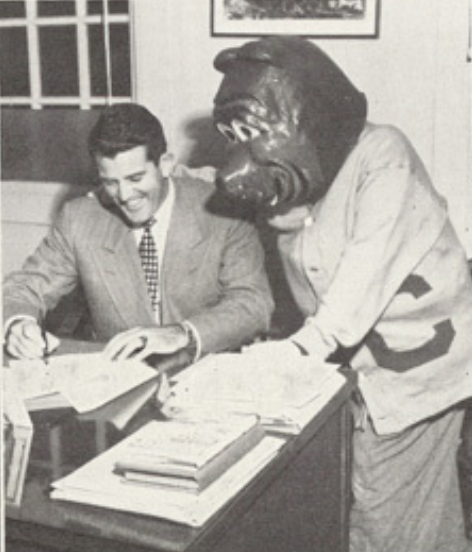 Archival scan: Oski leaning over books at a desk. Photo credit: Photographer/artist uncredited in supplied scan.