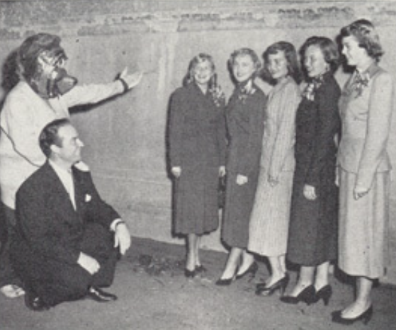 Archival scan: Oski with a group posing indoors. Photo credit: Photographer/artist uncredited in supplied scan.
