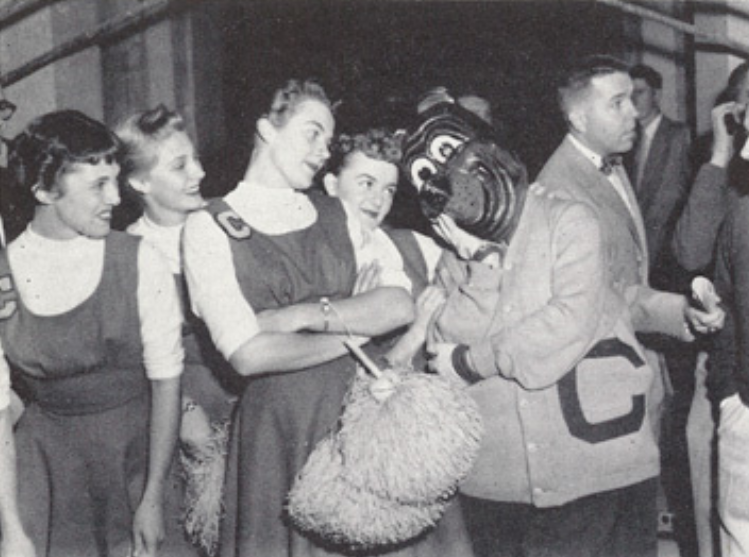 Archival scan: Oski holding a basket beside a group. Photo credit: Photographer/artist uncredited in supplied scan.