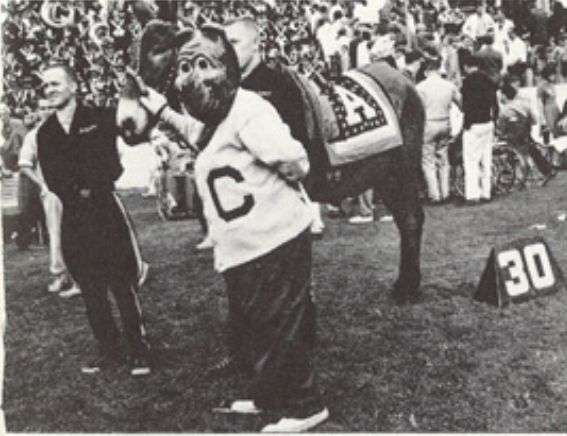 Archival scan: Oski beside a horse on the football field. Photo credit: Photographer/artist uncredited in supplied scan.