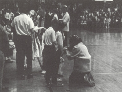 Archival scan: Oski kneeling beside basketball officials. Photo credit: Photographer/artist uncredited in supplied scan.