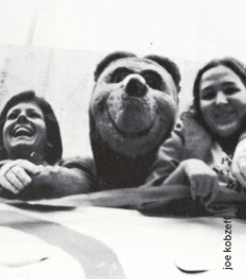 Archival scan: Oski and two fans leaning over a railing. Photo credit: Joe Klotz (printed scan credit).