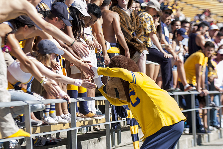 Oski greeting fans leaning over the stadium railing. Photo credit: Keegan Houser / UC Berkeley.